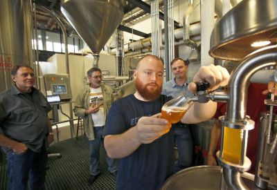 Seattle, Wa. August 16, 2014.
From left, Wayne Carpenter, and Bob Rock from Skagit Valley Malting Company, and Emerson Lamb, at right, co-founder, Westland Distillery, watch as Matt Hofmann, master distiller, at Westland Distillery draws the first sample of a wort made from barley grown and malted in the Skagit Valley.