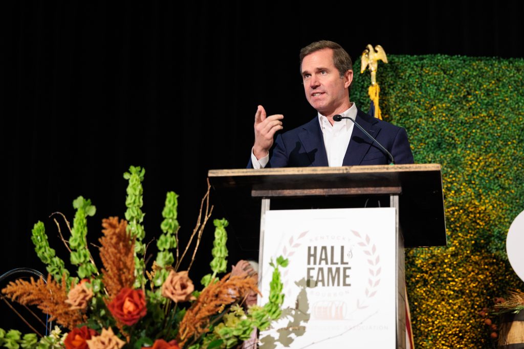 Governor Andy Beshear speaking at the podium during the 2026 Kentucky Bourbon Hall of Fame Induction Ceremony